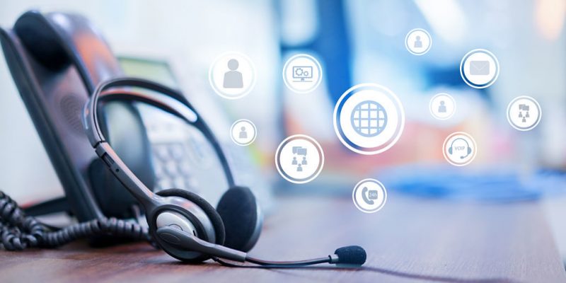 close up focus on call center headset device at VOIP system on telephone machine with virtual interface of communication at office desk for hotline telemarketing and network operation concept